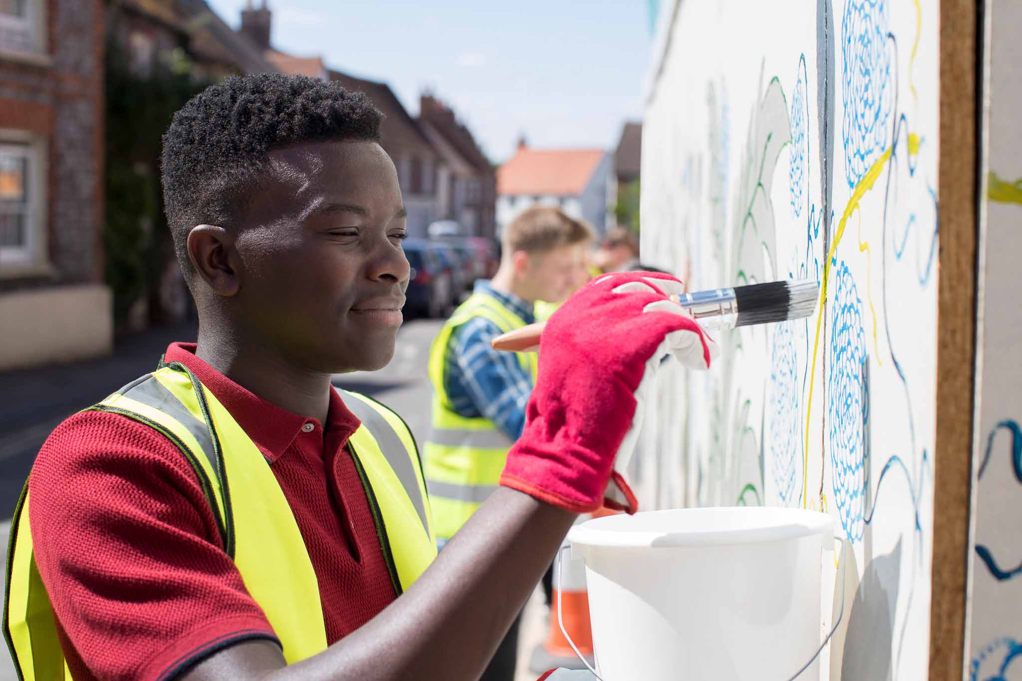 Teenagers paint a colorful mural on a sunny street, and have all the tools and gear to do the job perfectly.