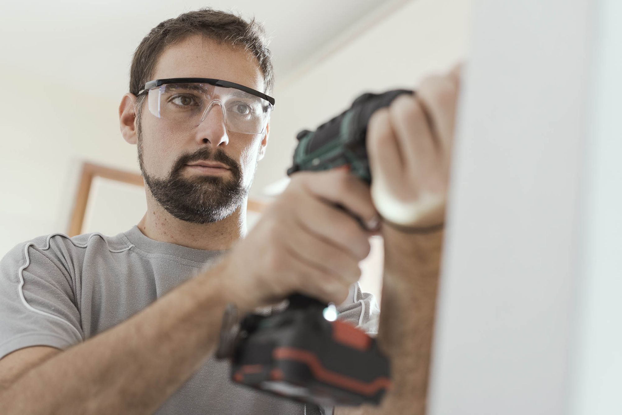 A man wearing protective goggles happily uses an electric drill to make the holes necessary to install a tablet mount. 