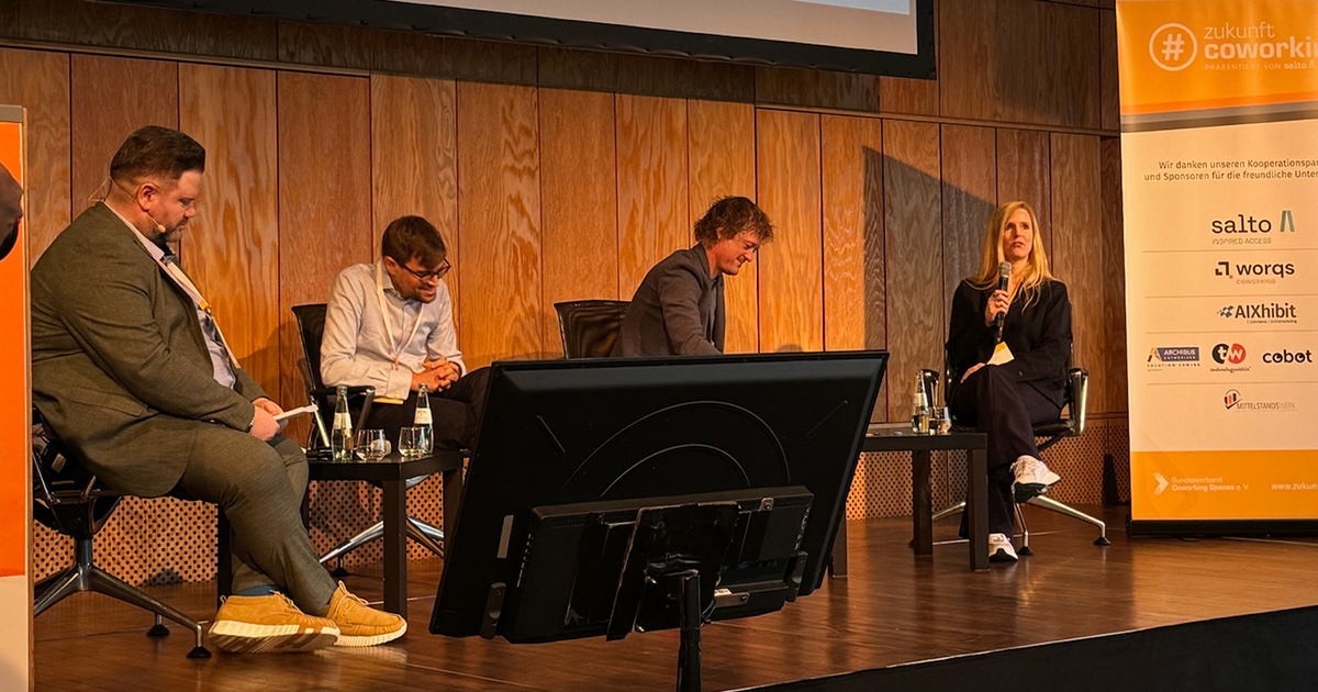 A panel discussion at ZukunftCoworking 2024, featuring four participants on stage. Laura Tump from Cobot speaks into a microphone, seated to the right. Other panelists include Christian Schmitz and Florian Kappes. A ZukunftCoworking banner and sponsor logos, including Cobot, are visible on the right side of the stage.