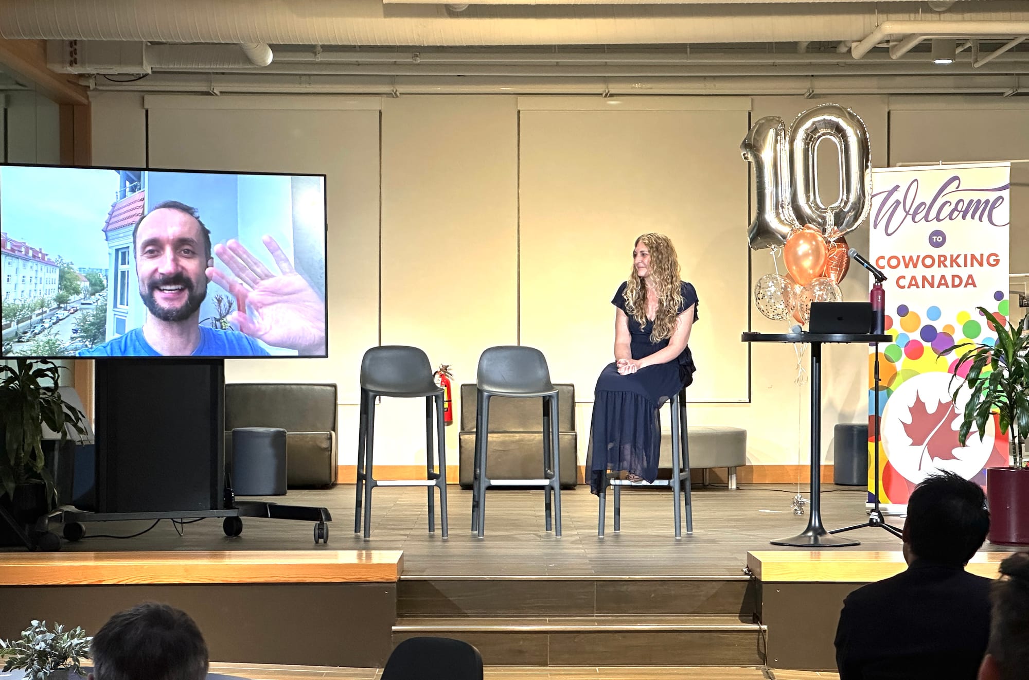 Ashley Proctor from Creative Blueprint pays tribute to Cobot’s CEO, Thilo Utke, who is seen on a large screen waving from a remote location during the Coworking Canada Unconference 2024.