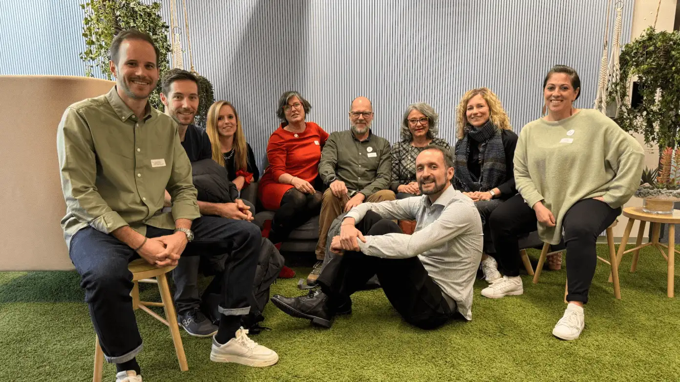 8 people sitting on chairs and Thilo Utke from Cobot sitting in the middle on the ground. Pictured in the Coworking Switzerland 2025 conference.